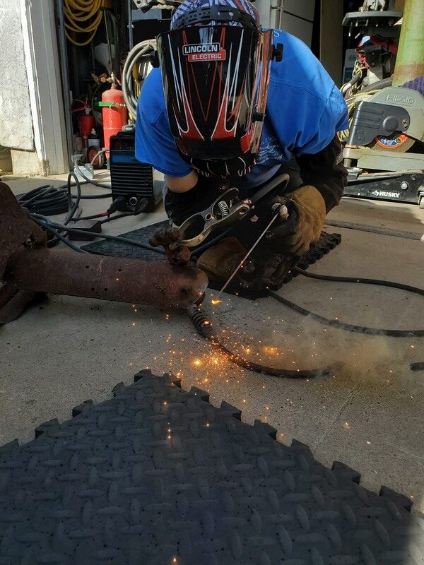 Dave mid-weld on a trailer part in the driveway